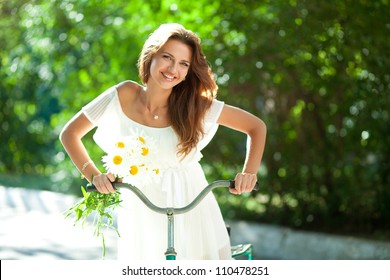 Young Woman In A White Summer Dress And Daisies In Her Hand Clinging To An Old Bicycle Handlebars