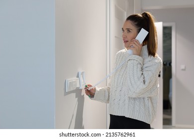 Young woman in a white sweater answers the intercom in the hallway