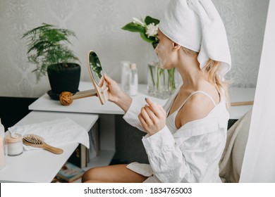 Young woman in white towel chilling in bedroom and making clay facial mask near mirror. Girl doing beauty treatment and relaxing at home. Morning skin care beauty routine, self care - Powered by Shutterstock