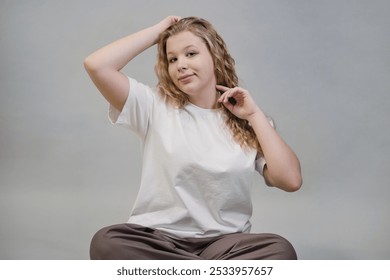 A young woman in a white t-shirt, oversized black denim jacket, and beige pants stretches her arms forward while seated against a neutral backdrop. This image highlights casual streetwear style and - Powered by Shutterstock