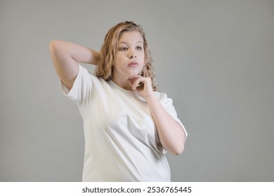 A young woman in a white t-shirt, oversized black denim jacket, and beige pants stretches her arms forward while seated against a neutral backdrop. This image highlights casual streetwear style and - Powered by Shutterstock