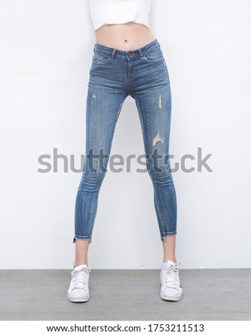 Young woman in white vest with fashionable denim torn, jeans and white sneaker shoes on gray background 

