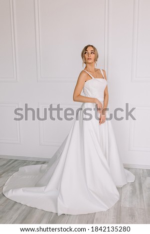 Young woman in a white wedding dress with long hair before the engagement ceremony on a white background with a model appearance important wife for the bride posing in front of the photographer	