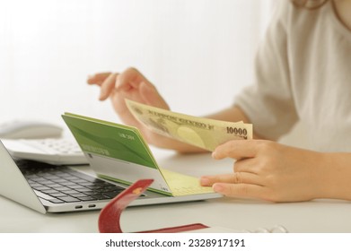 A young woman who calculates money.

The passbook held by a woman is listed as "savings account" in Japanese. - Shutterstock ID 2328917191