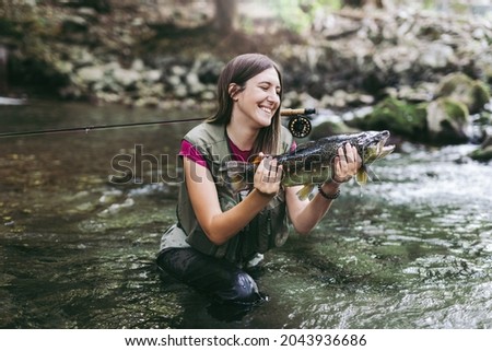 A young woman, who does sports fishing, fishes on a fast mountain river and holds a trout she caught in her hand. 