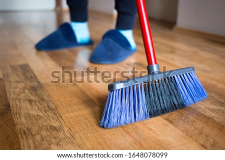 Young woman, wife in blue slippers using indoor blue broom for hardwood floor cleaning. Spring cleaning concept