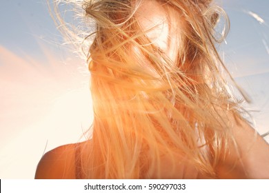 Young woman with windy messy hair backlit by sun selective focus toned image, sun flares