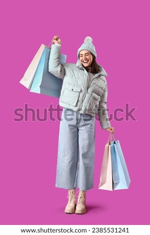 Young woman in winter clothes with shopping bags on purple background