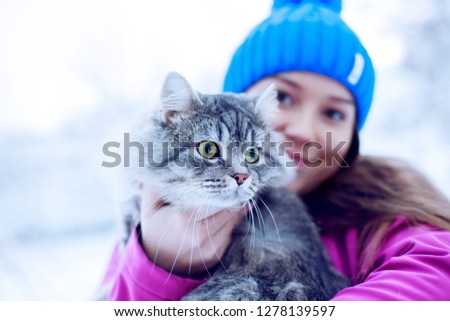 Young woman in winter park holding, hug her lovely fluffy cat. Girl and her gray cute kitten walking together outdoor. Seasons, pets, friendship, lifestyle concept. Friend of human. Snowy winter day.