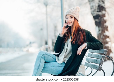 Young Woman In Winter Park Talking Mobile Phone, Sitting On The Bench