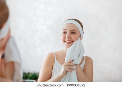 Young woman wipes herself face with white towel after shower washing. Self care in morning at bathroom. Happy smiling teenage girl do morning routine daily hygiene. Portrait reflection in mirror - Powered by Shutterstock