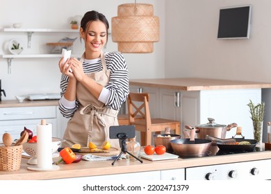 Young woman wiping her hands with paper towel while watching cooking video tutorial in kitchen