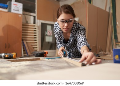 Young woman woodworker with wooden board behind workbench