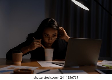 The young woman worked late and is now eating instant noodles at the office - Powered by Shutterstock