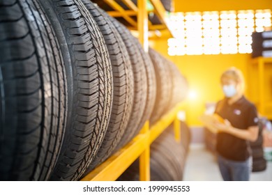 A Young Woman Worker With A Clipboard Checking Stocks Of New Tires Ready To Be Replaced At A Service Center Or Tire Shop. The Background Is A Warehouse. Stock New Tires For The Car Industry.