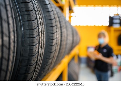 A Young Woman Worker With A Clipboard Checking Stocks Of New Tires Ready To Be Replaced At A Service Center Or Tire Shop. The Background Is A Warehouse. Stock New Tires For The Car Industry.