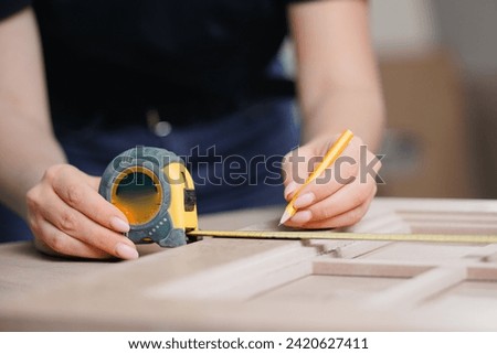 Young woman worker marks with pencil dimensions of wooden furniture for cutting on machine. DIY Small Business Production of kitchen.