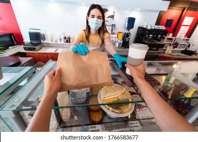 Young woman worker serving takeaway breakfast inside bar cafeteria while wearing face safety mask during coronavirus outbreak - Prevention measure and food concept - Focus on right hand holding coffee