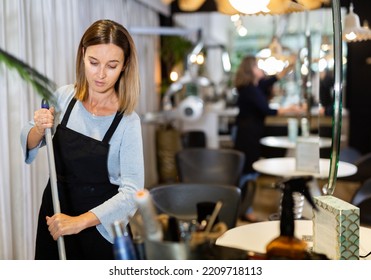 Young Woman Working In Barber Shop, Cleaning Workplace, Sweeping Floor .