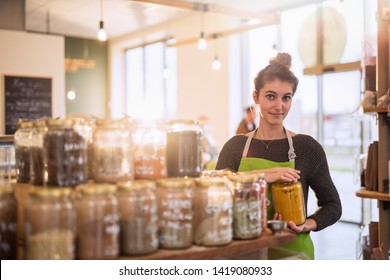 Young Woman Working In A Bulk Food Store, She Puts Away The Spice Jars