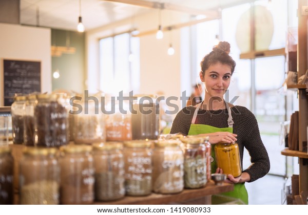 Young woman working in a bulk food store, she puts\
away the spice jars