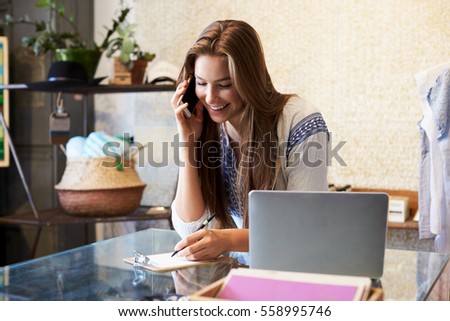 Young woman working in clothing store takes a phone enquiry