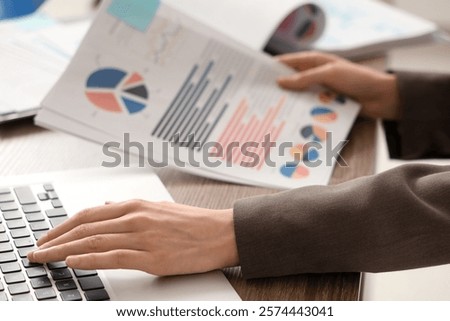 Young woman working with documents while using laptop in office. Closeup