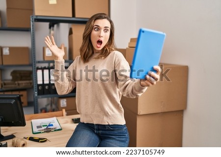 Young woman working ecommerce doing video with tablet scared and amazed with open mouth for surprise, disbelief face 
