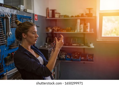 Young Woman Working In Factory. Beautiful Lady At Work In Her Workshop. Young Smiling Mechanic Checks Her Tools. Portrait Of Young Female Mechanic