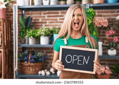 Young woman working at florist holding open sign angry and mad screaming frustrated and furious, shouting with anger looking up.  - Shutterstock ID 2363789333