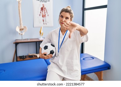 Young Woman Working At Football Therapy Clinic With Angry Face, Negative Sign Showing Dislike With Thumbs Down, Rejection Concept 