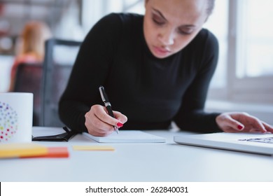 Young woman working at her desk taking notes. Focus on hand writing on a notepad. - Shutterstock ID 262840031