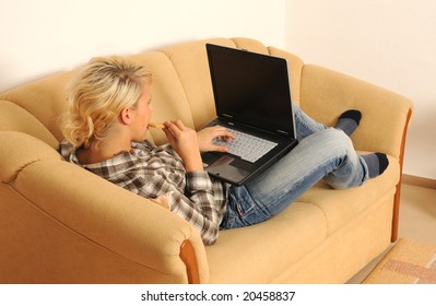 Young woman working with her laptop, sitting on a sofa.