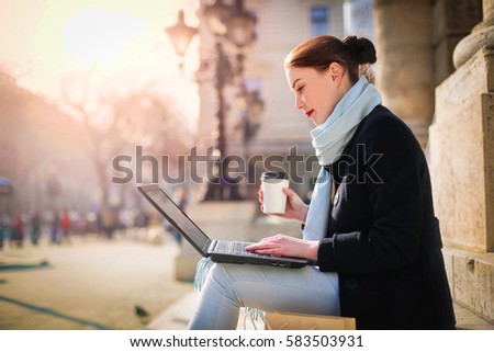 Young woman working with her laptop, sitting on stairs in the street