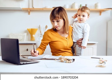 Young woman working at home with a laptop with a baby on his hands. Stay home concept. Home office with kids. Mother is working from home.