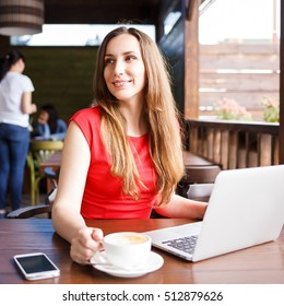 Young woman working with laptop and cup of cappuccino in cafe having coffee break