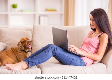 Young Woman Is Working With Laptop And Her Dog Sitting On Sofa Near.
