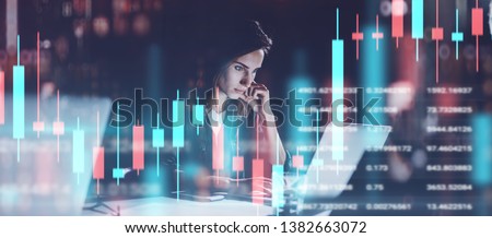 Young woman working at night modern office.Technical price graph and indicator, red and green candlestick chart and stock trading computer screen background. Double exposure.Wide