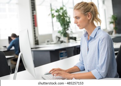 Young Woman Working In Office Sitting At Desk. Beautiful Blonde Businesswoman Typing And Writing A Email On Computer. Young Assistant Completing Pending Work In Office.