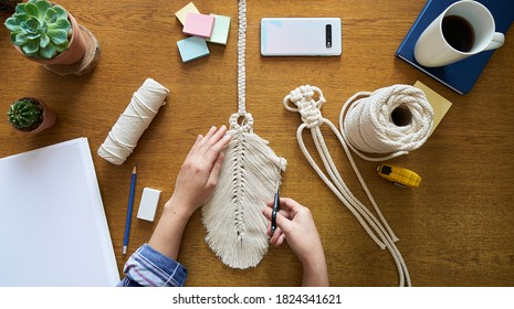 A young woman working on custom macrame decor with tools over a creative desktop watched from above