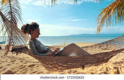 Young Woman Working On Laptop Lying In Hammock At Sand Beach Of Tropical Island. Freelance Outdoor Work Concept