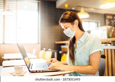 Young Woman Working On Laptop, Wearing Protective Face Mask.Online Training Education And Freelance Work.Studying Remotely.Outsourcing. Coronavirus Pandemic Concept