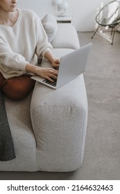 Young woman working on laptop computer sitting on comfortable sofa. Aesthetic work at home freelancer concept. Elegant girl boss, lady boss business composition for blog, web, social media