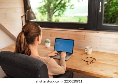 Young Woman Working On Laptop Computer In A Home Modern Office Setting With A Relaxing Green Nature View. 