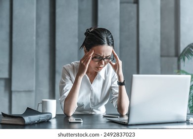 Young woman working on laptop having headache. Bored workaholic female accountant employee with headache and stress. Businesswoman woman with migraine, stress relief, chronic pain - Powered by Shutterstock