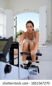 Young Woman Working Out With A Rowing Machine At Her Home Gym With The Focus On The Woman In The Background