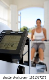 Young Woman Working Out With A Rowing Machine At Her Home Gym With The Focus On The Machine's Display