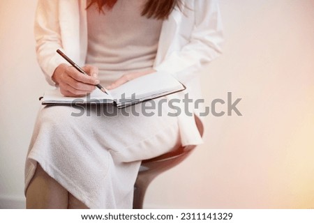 A young woman, working as a psychotherapist, carefully listens to her patient and jots down notes in her notebook. The session focuses on therapy.