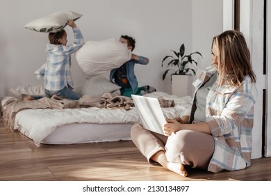 Young Woman Is Working Remotely On A Laptop At Home, Mom Is Working, Children Are Making Noise. Home Office Workplace, Remote Work, E-learning Concept, Home Schooling, Freelance