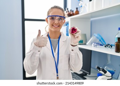 Young Woman Working At Scientist Laboratory Holding Geode Smiling Happy And Positive, Thumb Up Doing Excellent And Approval Sign 